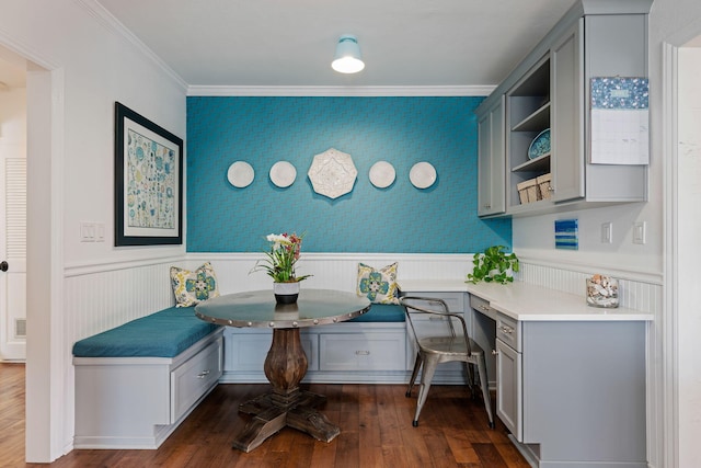 office space with crown molding, a wainscoted wall, dark wood finished floors, and built in desk