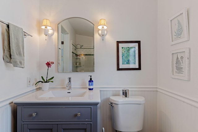 bathroom with wainscoting, a shower, vanity, toilet, and a decorative wall