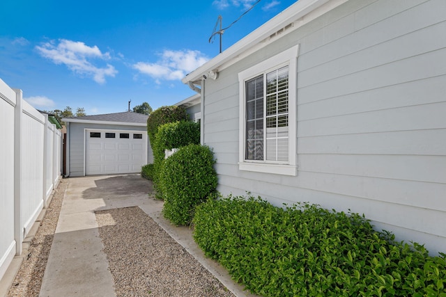 view of property exterior with a detached garage, fence, driveway, and an outbuilding