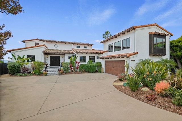 mediterranean / spanish-style home featuring a garage, stucco siding, a tiled roof, and concrete driveway