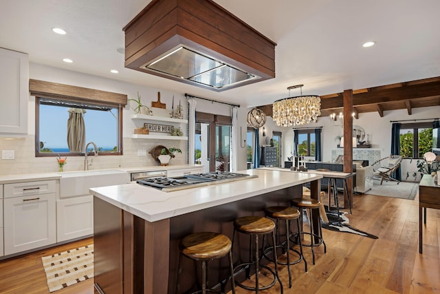 kitchen featuring decorative backsplash, a center island, white cabinets, a sink, and stainless steel gas stovetop