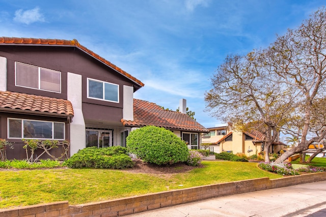 view of front facade featuring stucco siding, a tile roof, and a front yard