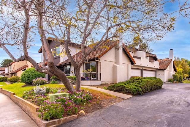 view of side of property with a tiled roof, a chimney, driveway, and stucco siding