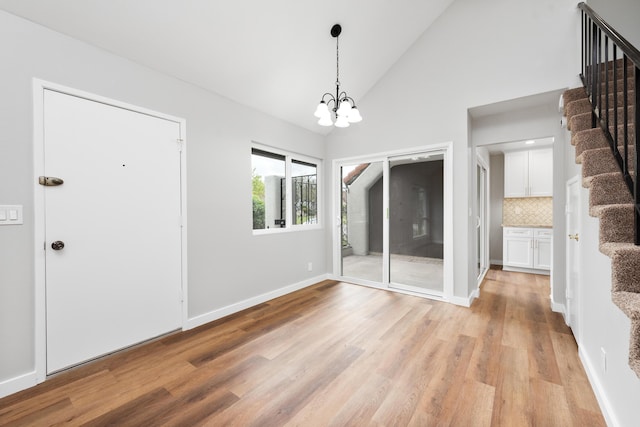 unfurnished dining area featuring an inviting chandelier, baseboards, high vaulted ceiling, stairway, and light wood-style flooring