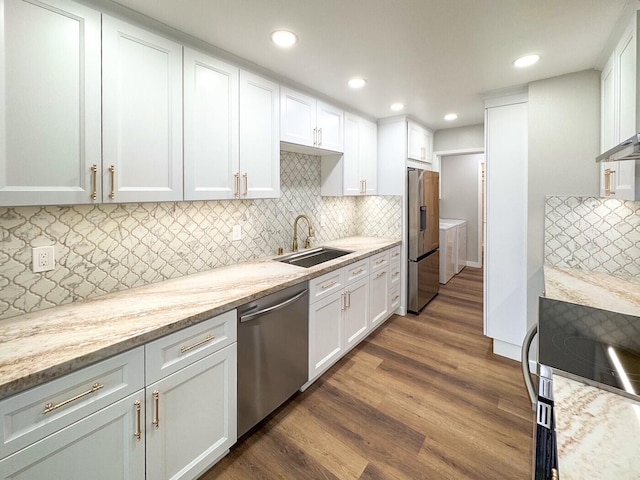 kitchen with washing machine and clothes dryer, a sink, stainless steel appliances, white cabinetry, and decorative backsplash