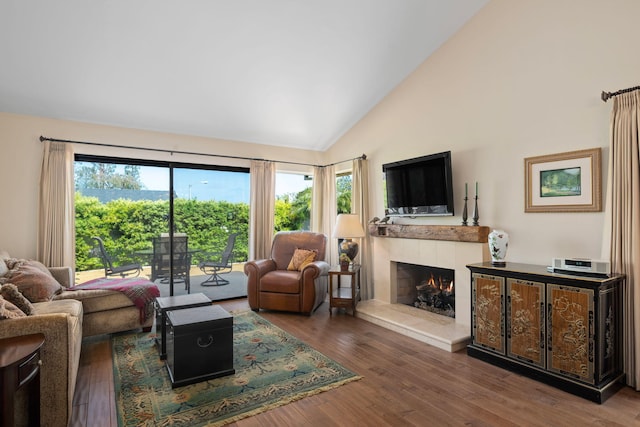 living room with high vaulted ceiling, wood finished floors, and a tile fireplace