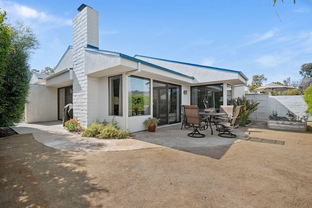 rear view of house featuring fence, a patio, stucco siding, and a chimney