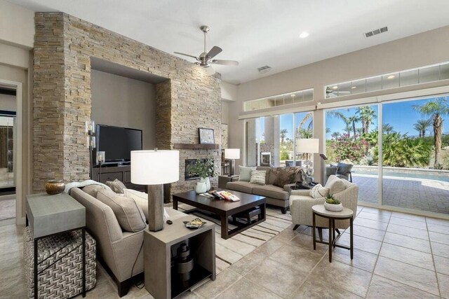 living room featuring a towering ceiling, ceiling fan, a fireplace, and visible vents