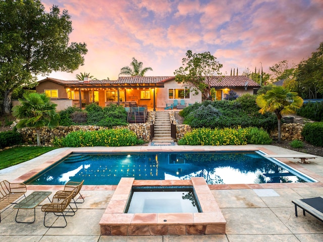 pool at dusk featuring an in ground hot tub, a diving board, an outdoor pool, a patio area, and stairs