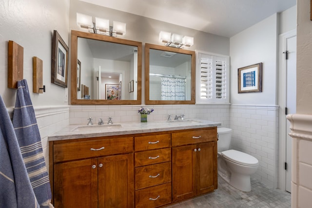 full bath with a sink, tile walls, toilet, and double vanity