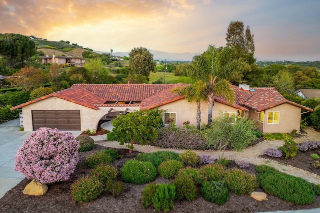 view of front of property featuring stucco siding, a chimney, driveway, and a tiled roof
