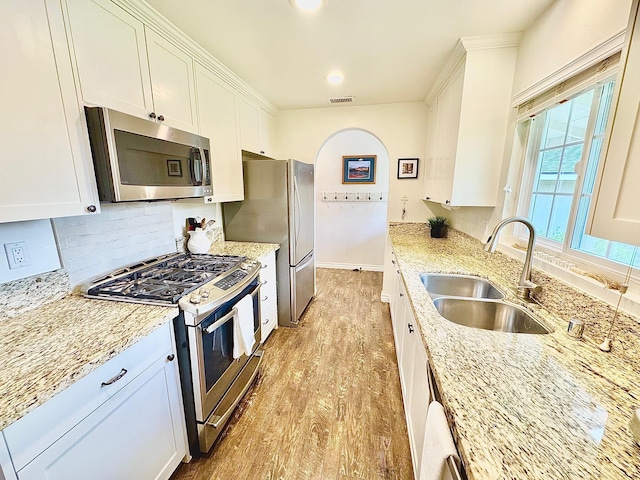 kitchen featuring white cabinets, appliances with stainless steel finishes, light stone counters, a sink, and light wood finished floors