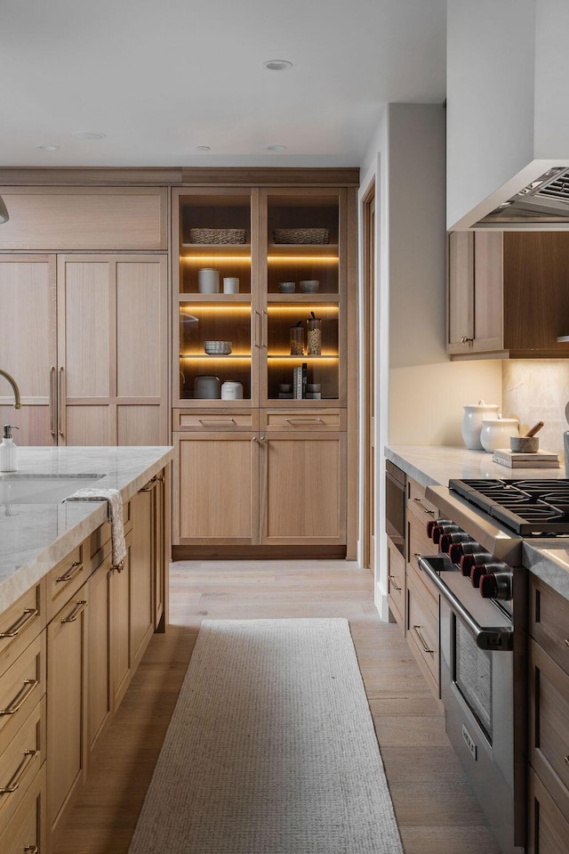 kitchen with light stone countertops, high end stainless steel range, a sink, light wood-style flooring, and range hood