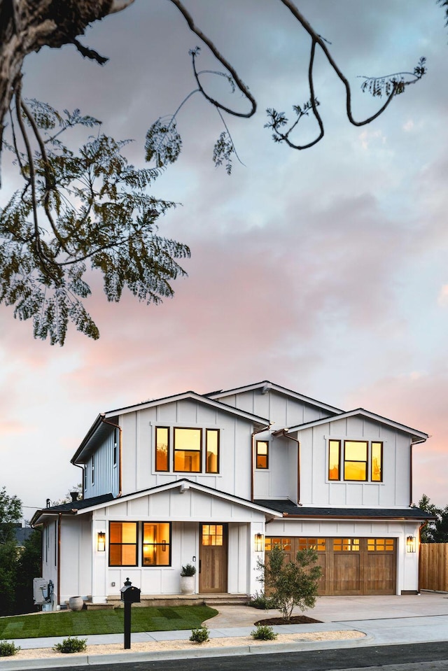 back of property at dusk with a lawn, fence, board and batten siding, concrete driveway, and an attached garage