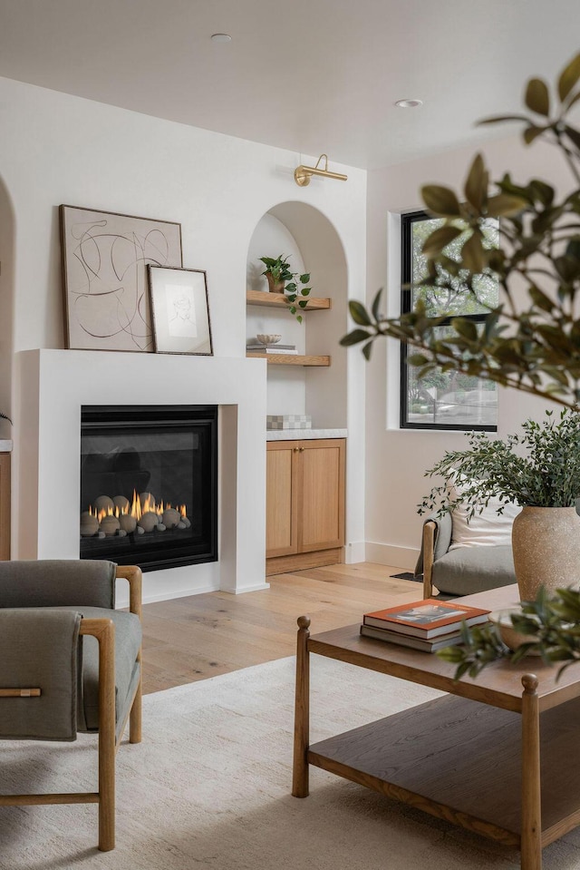 living room featuring a glass covered fireplace, baseboards, and light wood-style floors