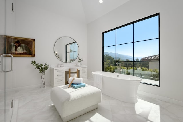 bathroom featuring marble finish floor, a freestanding tub, high vaulted ceiling, and a mountain view