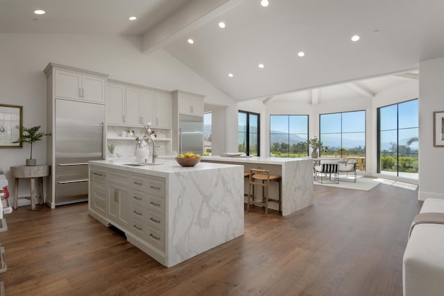 kitchen featuring a sink, beam ceiling, a center island with sink, dark wood-style flooring, and built in fridge