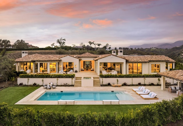 back of house featuring a tiled roof, outdoor lounge area, a fenced in pool, and a lawn