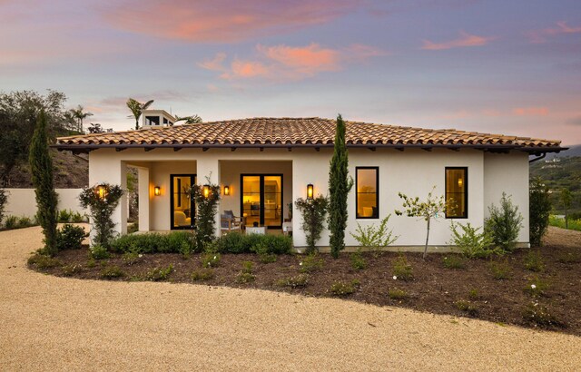 mediterranean / spanish-style house with covered porch, a tiled roof, stucco siding, and fence