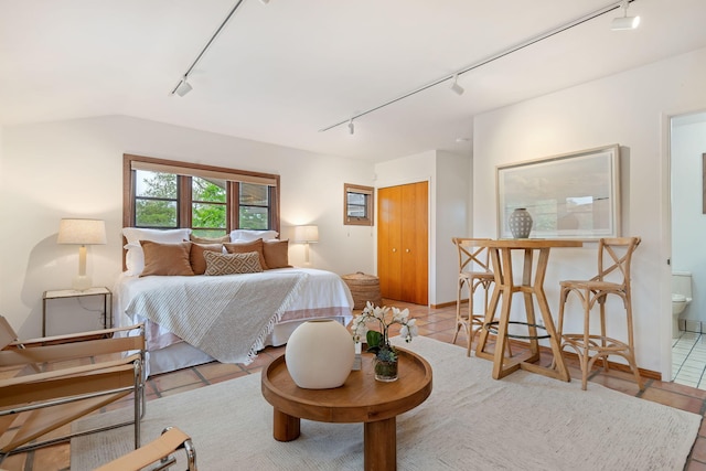 bedroom with ensuite bath, light tile patterned floors, and track lighting