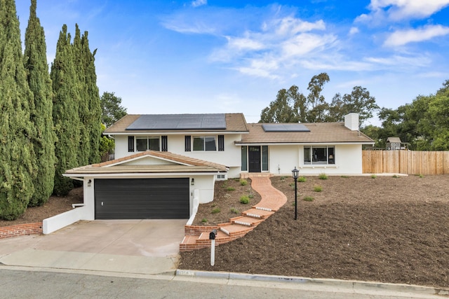 tri-level home featuring roof mounted solar panels, stucco siding, a chimney, fence, and concrete driveway