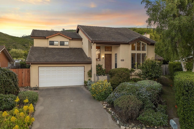 view of front of home with an attached garage, stucco siding, driveway, and fence
