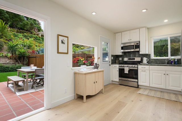 kitchen featuring appliances with stainless steel finishes, light wood-type flooring, backsplash, white cabinets, and a sink