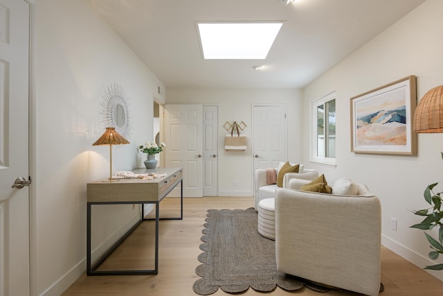 living area with a skylight, light wood finished floors, and baseboards