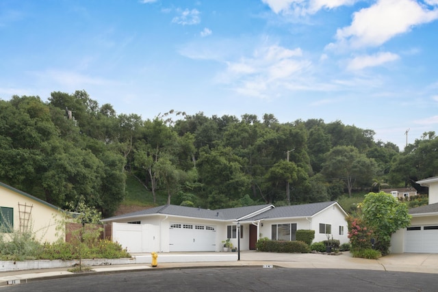 ranch-style home featuring stucco siding, an attached garage, concrete driveway, and a forest view