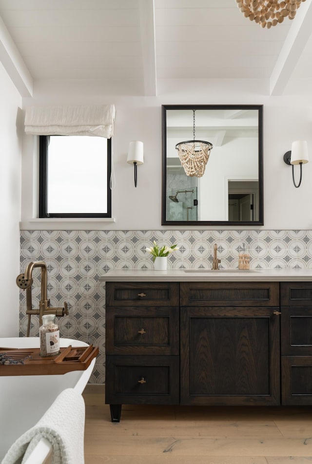 bathroom with an inviting chandelier, wood finished floors, a soaking tub, beamed ceiling, and vanity