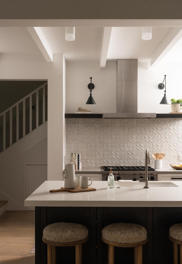 kitchen featuring a breakfast bar area, range hood, decorative backsplash, wood finished floors, and beamed ceiling