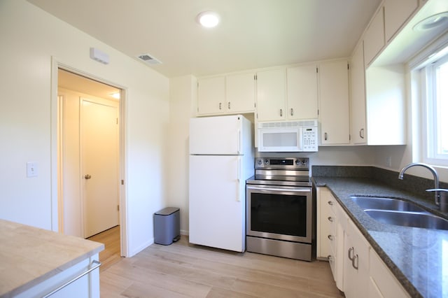 kitchen with white appliances, a sink, light wood-style floors, white cabinetry, and dark stone counters