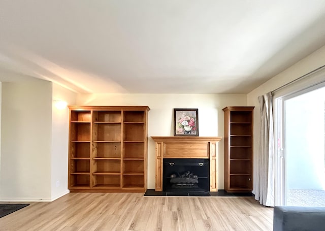 unfurnished living room featuring light wood-type flooring, a fireplace with raised hearth, and baseboards