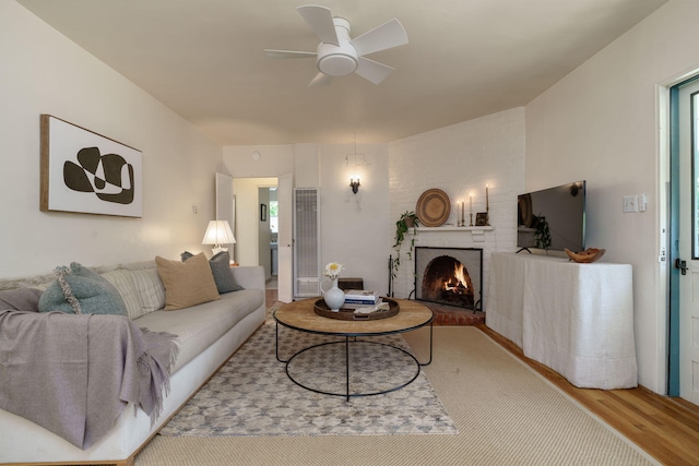 living area featuring wood finished floors, a heating unit, a ceiling fan, and a brick fireplace
