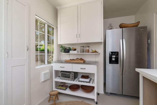 kitchen with stainless steel fridge, open shelves, white cabinetry, and baseboards