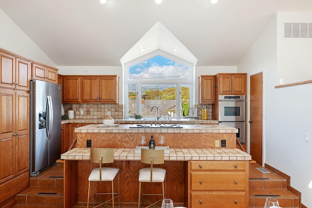 5529 Calle Arena, Carpinteria, CA 93013 - kitchen featuring stainless steel appliances, vaulted ceiling, tile counters, tasteful backsplash, and a kitchen island