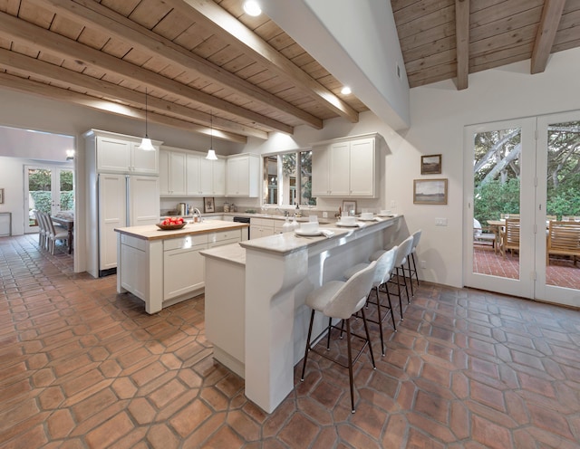 603 Juan Crespi Ln, Montecito, CA 93108 - kitchen featuring wooden ceiling with exposed beams, a kitchen island with sink, a peninsula, a kitchen breakfast bar, and white cabinets