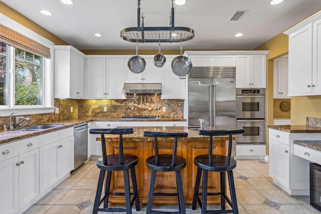 5049 Via Lara Ln, Santa Barbara, CA 93111 - kitchen with stainless steel appliances, under cabinet range hood, white cabinetry, light tile patterned floors, and backsplash