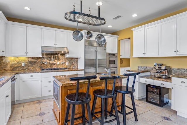 5049 Via Lara Ln, Santa Barbara, CA 93111 - kitchen with under cabinet range hood, built in appliances, white cabinetry, light tile patterned floors, and recessed lighting