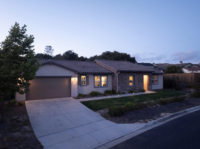 view of front facade with a tiled roof, a garage, a yard, driveway, and stucco siding