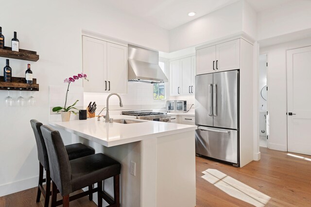 3736 State St Unit 109, Santa Barbara, CA 93105 - kitchen featuring stainless steel fridge, wall chimney exhaust hood, a peninsula, a sink, and light wood finished floors