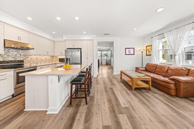 5696 Surfrider Way Unit 101, Goleta, CA 93117 - kitchen featuring appliances with stainless steel finishes, under cabinet range hood, light countertops, a kitchen breakfast bar, and light wood-style floors