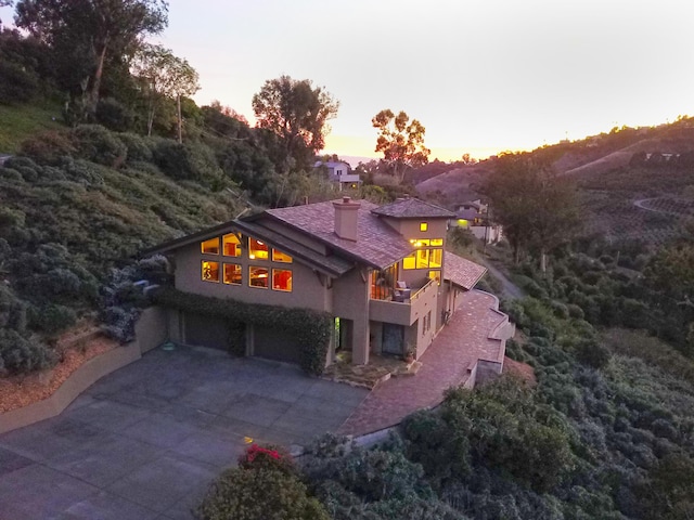 62 Canon View Rd, Montecito, CA 93108 - back of house at dusk with stucco siding, concrete driveway, an attached garage, a chimney, and a balcony