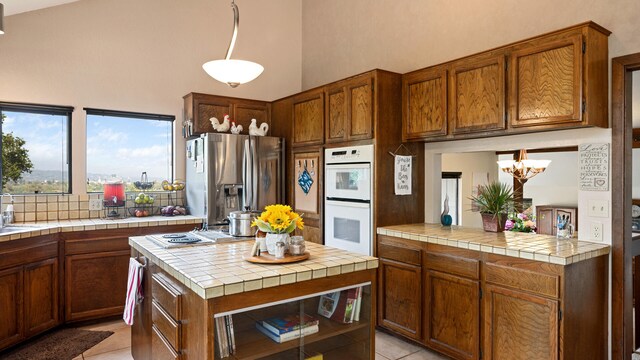 1010 Portesuello Ave, Santa Barbara, CA 93105 - kitchen with white double oven, light tile patterned flooring, a chandelier, stainless steel fridge with ice dispenser, and a high ceiling