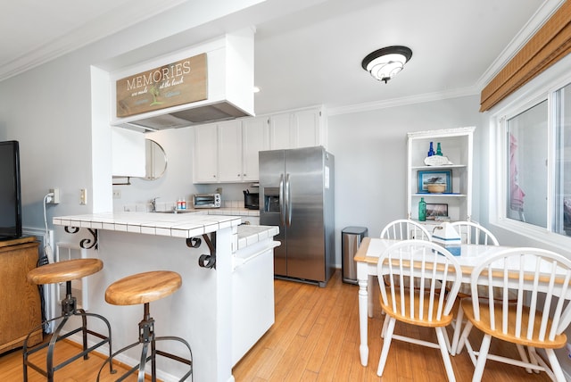 4975 Sandyland Rd Unit 302, Carpinteria, CA 93013 - kitchen featuring stainless steel fridge with ice dispenser, tile counters, white cabinetry, a peninsula, and ornamental molding