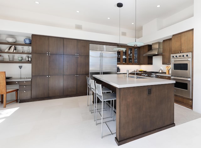 191 E Mountain Dr, Montecito, CA 93108 - kitchen with appliances with stainless steel finishes, wall chimney exhaust hood, a kitchen breakfast bar, dark brown cabinets, and light countertops