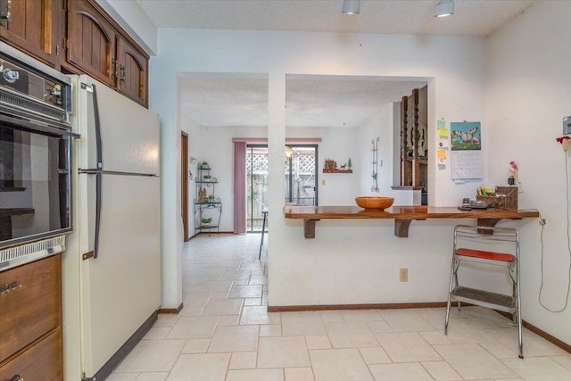 1300 E Airport Ave, Lompoc, CA 93436 - kitchen with freestanding refrigerator, black oven, a kitchen breakfast bar, a textured ceiling, and oven