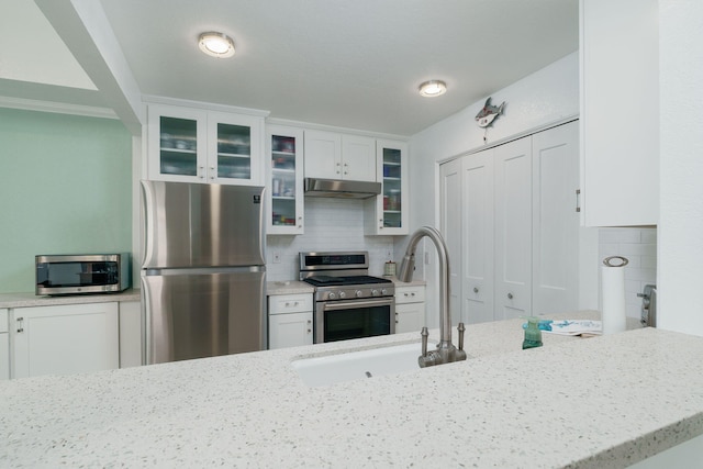 2206 Martinique Ln, Oxnard, CA 93035 - kitchen with appliances with stainless steel finishes, under cabinet range hood, white cabinetry, light stone countertops, and backsplash
