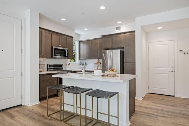 6594 Pipeline Pl, Goleta, CA 93117 - kitchen with appliances with stainless steel finishes, dark brown cabinetry, light wood finished floors, a breakfast bar area, and recessed lighting