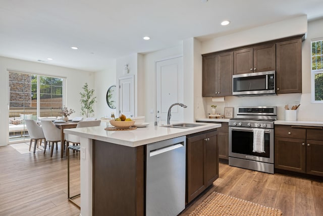 6594 Pipeline Pl, Goleta, CA 93117 - kitchen with appliances with stainless steel finishes, light countertops, dark brown cabinetry, a kitchen island with sink, and light wood finished floors